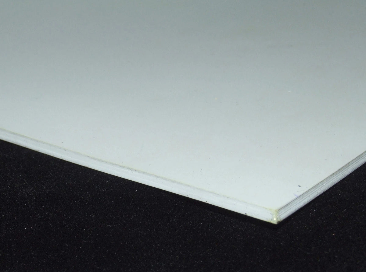 A close-up of a white rectangular panel or board resting on a black textured surface, showing a slight perspective angle and thin edge.