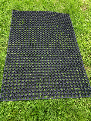 A black rubber mat with a raised circular grid pattern, laid flat on green grass.