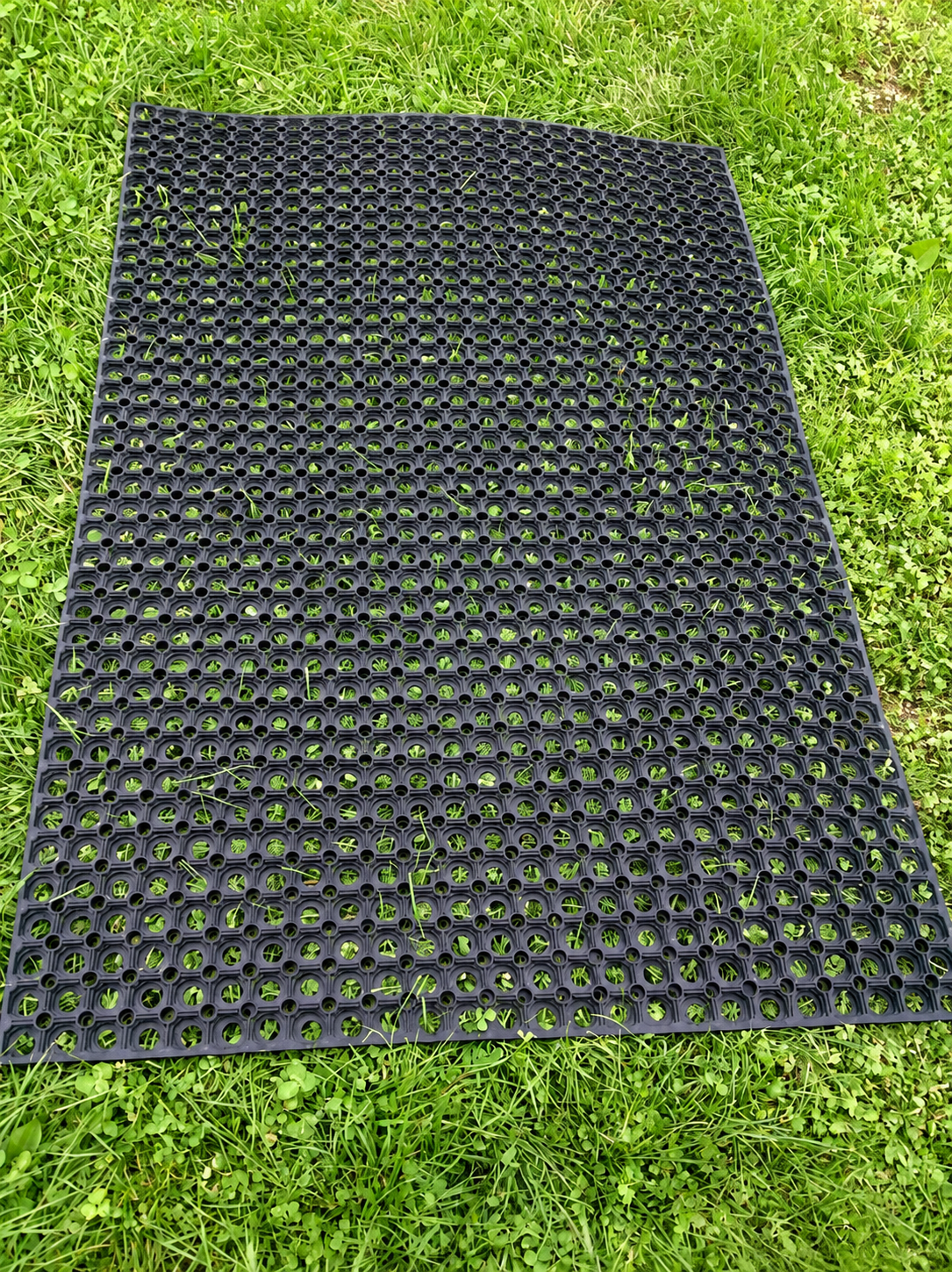 A black rubber mat with a raised circular grid pattern, laid flat on green grass.