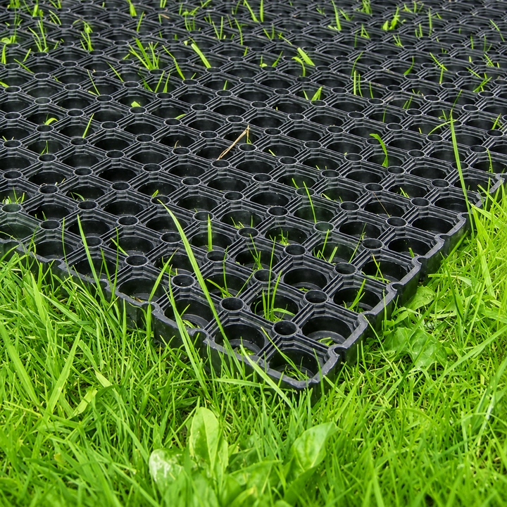 Black plastic hexagonal grid mat partially laid on bright green grass, showing the interlocking holes and textured surface.