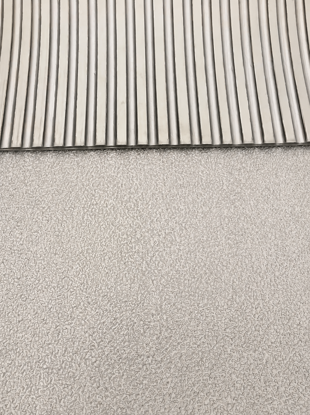 A close-up of a light gray textured material with a ribbed slatted pattern along the top edge.