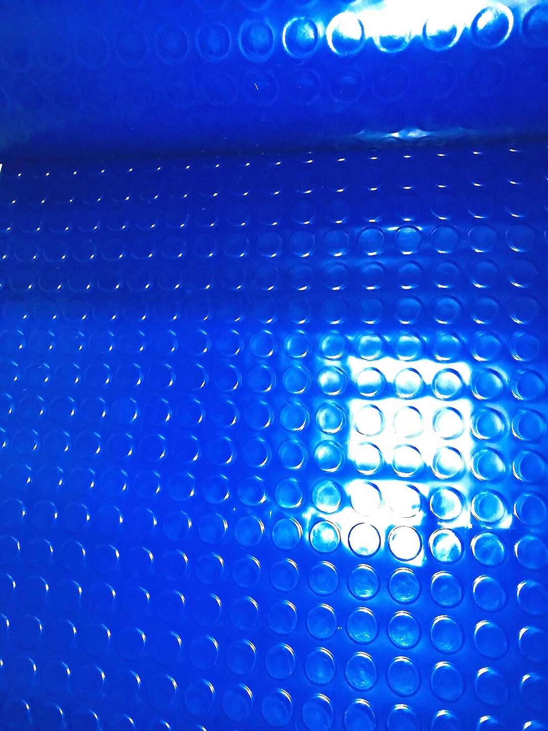 A close-up of a bright blue textured material with a repeating circular bubble or raised-dot pattern and glossy highlights.
