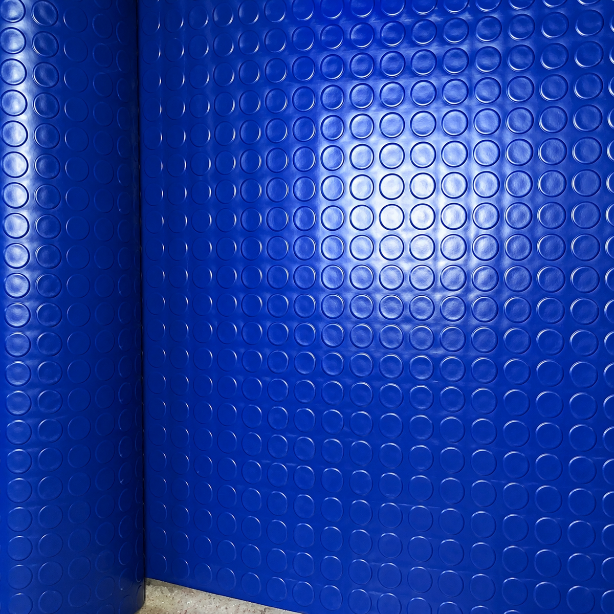 Blue textured wall panels with a repeating circular bubble pattern, shown installed in a corner with a light reflection in the center.
