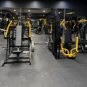 A gym interior showing multiple black and yellow weight machines and exercise equipment on a dark floor, with mirrors and ceiling lights visible in the background.