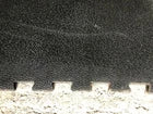 A close-up of a dark textured material, likely a black felt or foam pad, with a ribbed edge resting against a light gray textured surface.