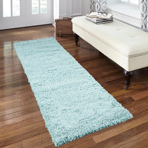 A long, light blue shag runner rug laid out on a dark wood floor in a bright room, with a cream tufted bench and white door visible in the background.