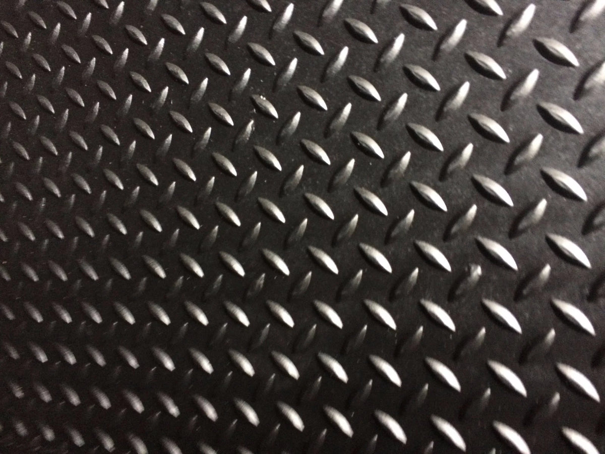 A close-up of a black diamond plate textured surface with repeating raised metallic oval shapes.