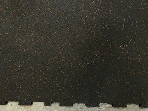 Black rubber interlocking foam floor tiles with small orange-brown flecks, showing a tongue-and-groove edge at the bottom.