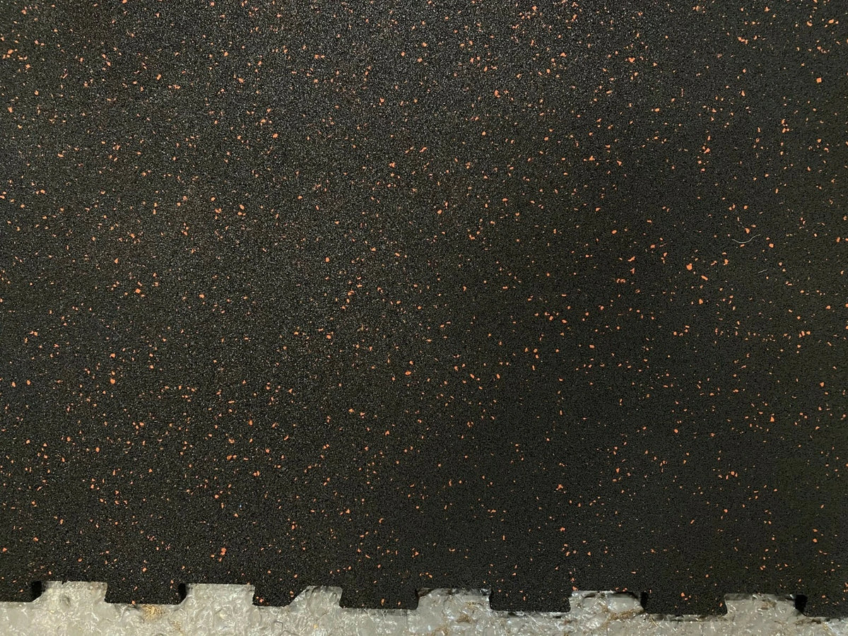 Black rubber interlocking foam floor tiles with small orange-brown flecks, showing a tongue-and-groove edge at the bottom.
