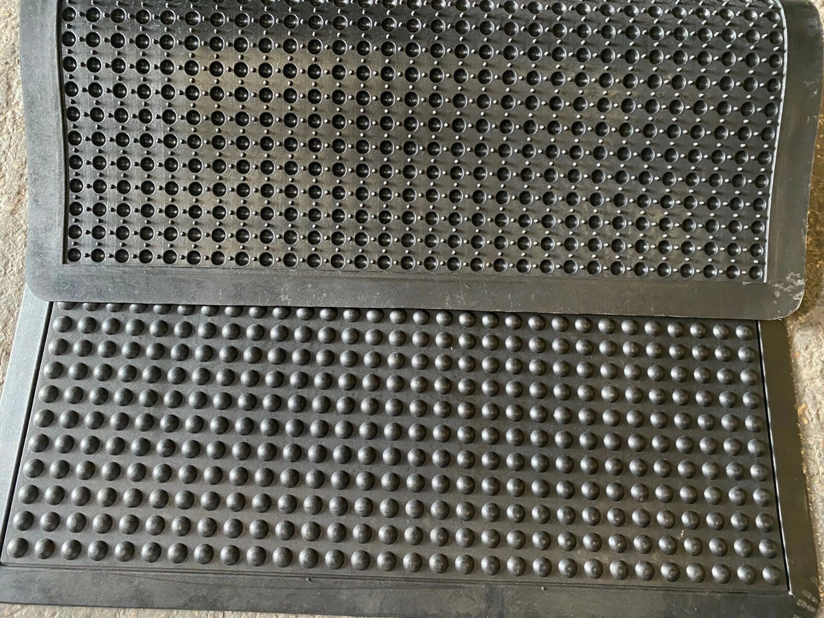 Two textured black mats with a grid pattern on a concrete floor.