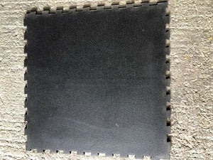 A black interlocking foam floor tile with a textured surface, shown against a light beige textured background.