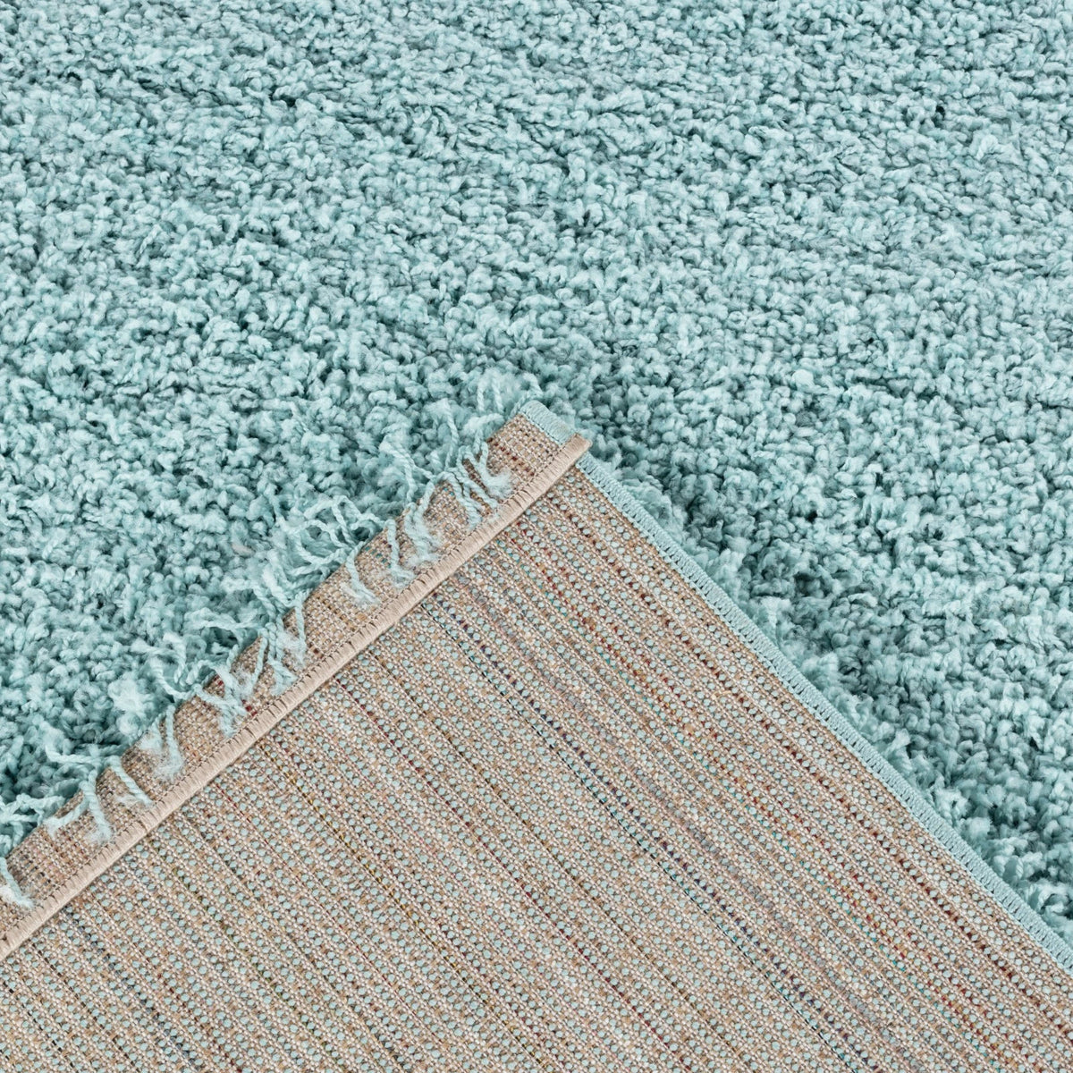 Close-up of a plush, high-pile shag rug in a light aqua or mint blue color, showing its thick textured fibers and a fringed edge with a woven backing.
