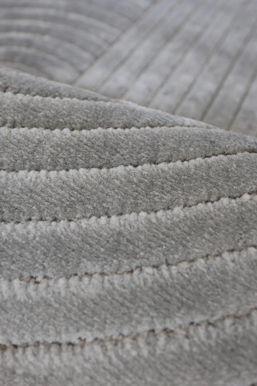 Close-up of a light gray ribbed fabric or carpet texture with stitched horizontal channels.