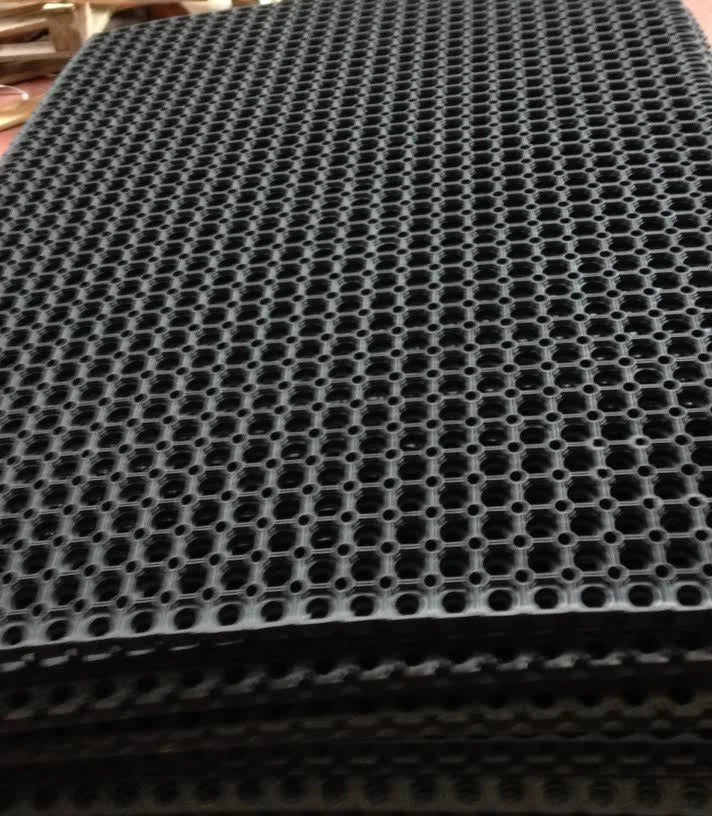 A close-up of a black plastic grid mat with a repeating honeycomb-style circular hole pattern, stacked on top of another mat.