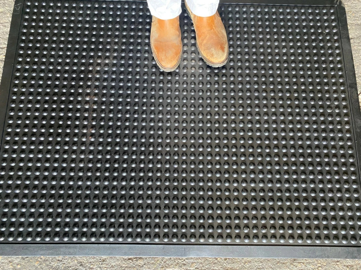 Person wearing shoes stepping onto a textured black mat