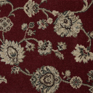 A close-up of a red area rug featuring a traditional floral pattern in beige and muted green.
