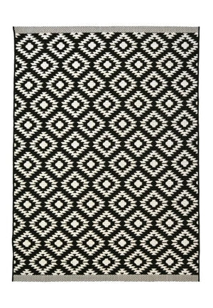 A rectangular woven rug with a black and off-white geometric diamond pattern, finished with a gray braided border.