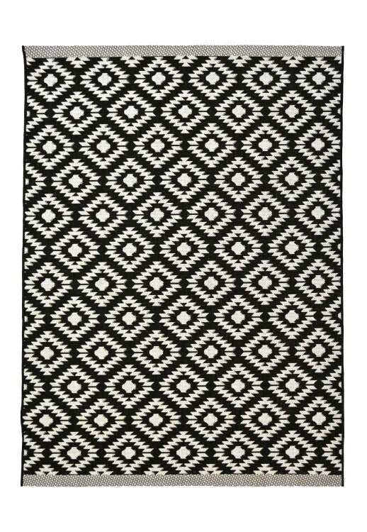 A rectangular woven rug with a black and off-white geometric diamond pattern, finished with a gray braided border.