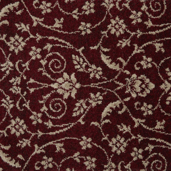 A close-up of a plush tufted rug with a deep burgundy red background and a cream-colored scrolling floral and vine pattern.