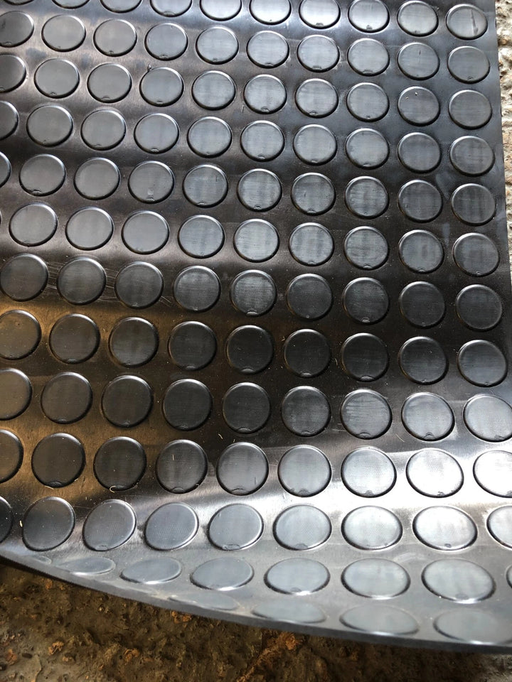 A close-up of a dark gray metallic sheet with a repeating pattern of raised circular domes, photographed against a rough concrete-like surface.