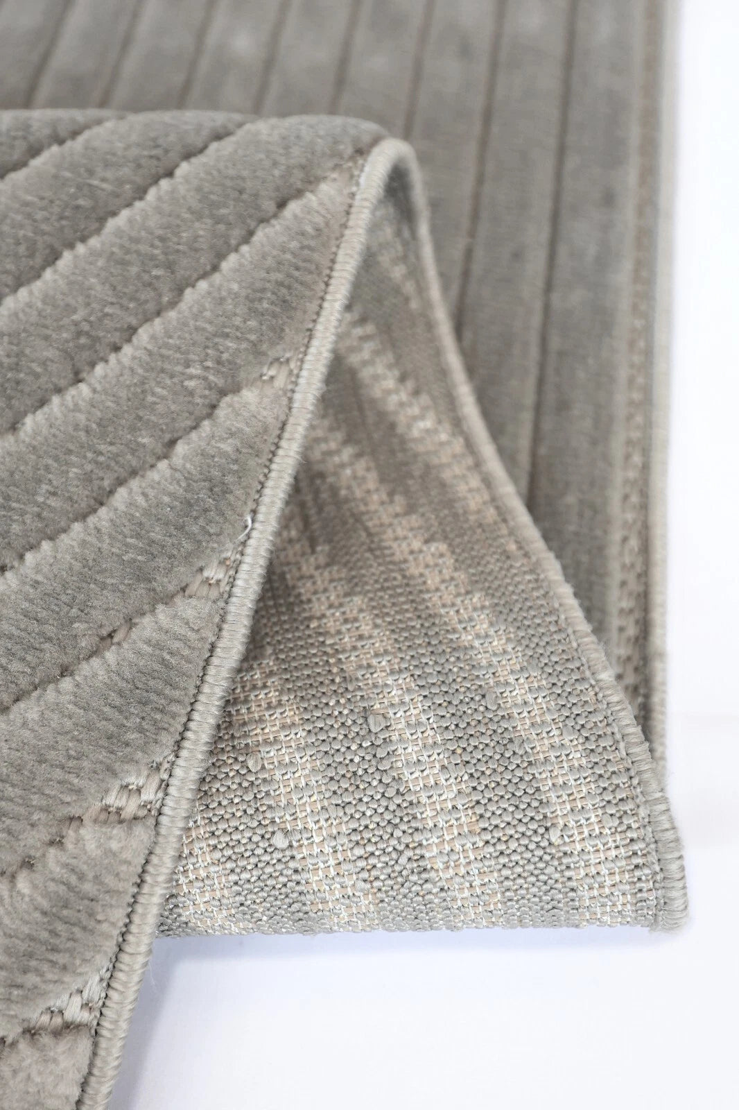 Close-up of a gray textured rug with a folded corner showing both its ribbed plush top and woven underside.