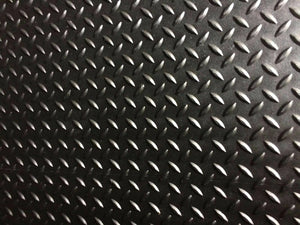 A close-up of a black diamond plate textured surface with repeating raised metallic oval shapes.