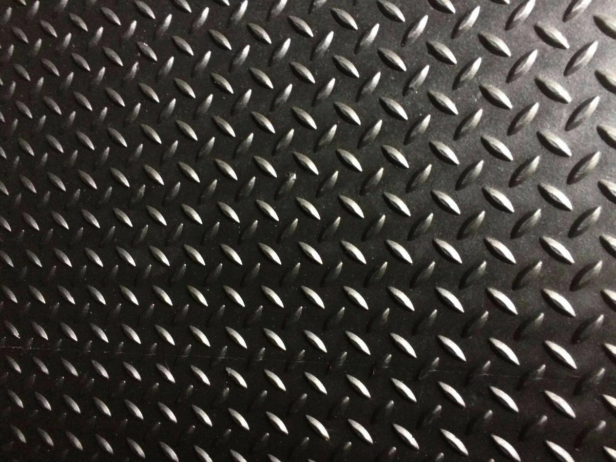A close-up of a black diamond plate textured surface with repeating raised metallic oval shapes.