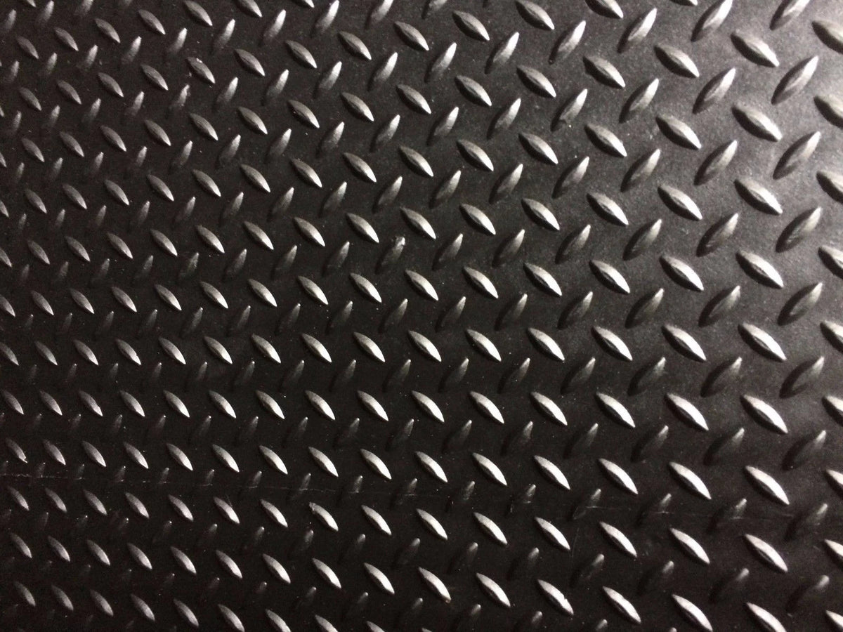 A close-up of a black diamond plate textured surface with repeating raised oval ridges.