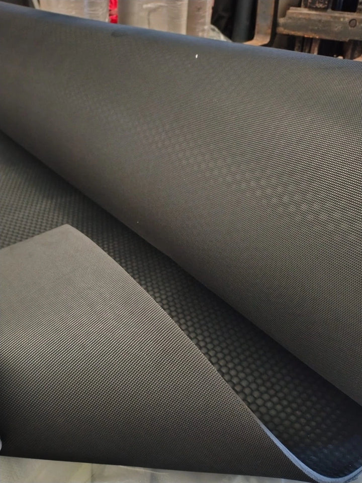 A close-up of a dark gray textured mat or carpet roll, partially unrolled to show its woven surface and backing.