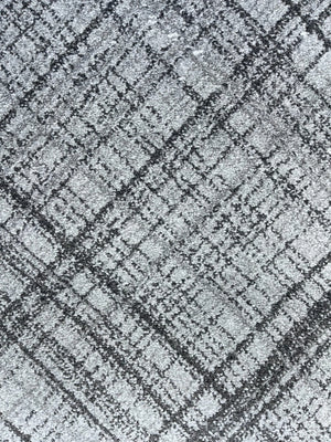 A close-up of a textured fabric or carpet pattern in gray and black, showing a distressed plaid or grid-like weave.