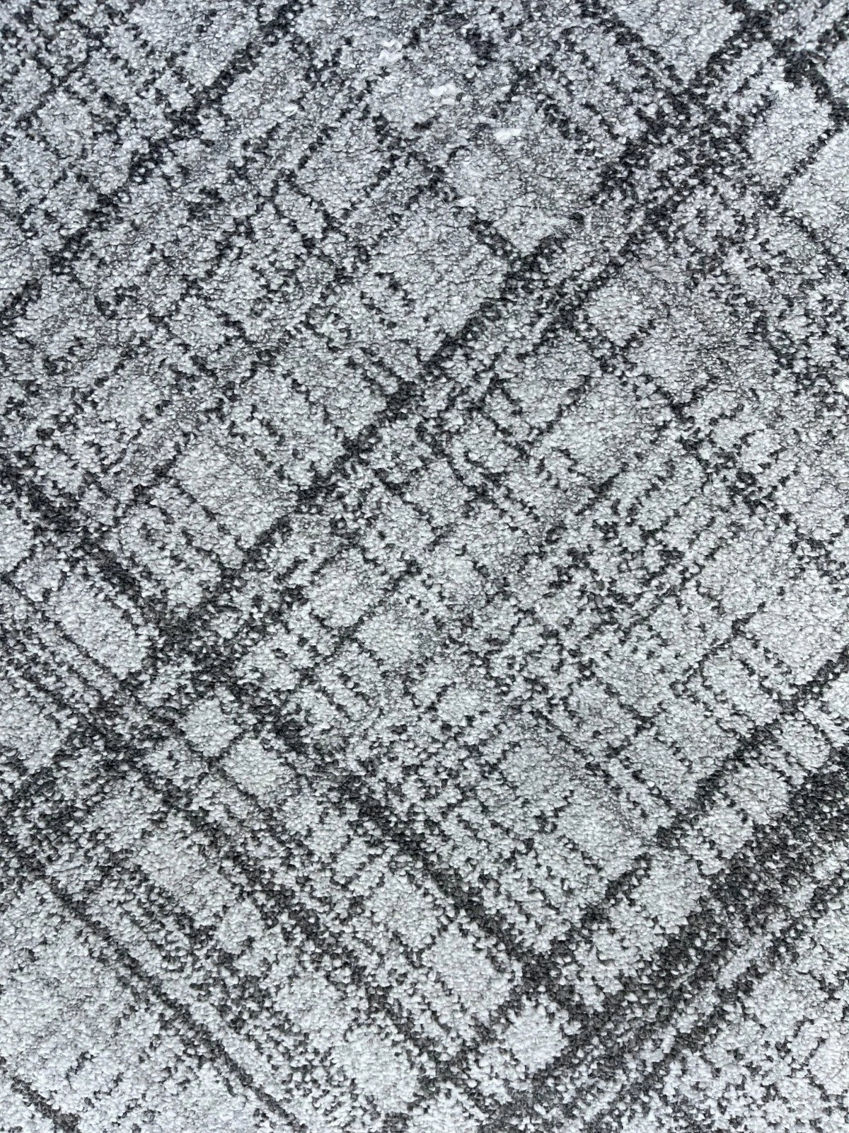 A close-up of a textured fabric or carpet pattern in gray and black, showing a distressed plaid or grid-like weave.