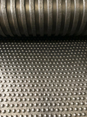 Close-up of a textured metal surface with a roll of metal pipe in the background.