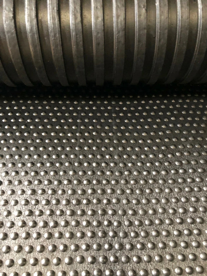 Close-up of a textured metal surface with a roll of metal pipe in the background.