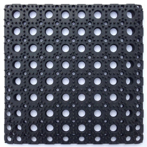 A square black rubber or plastic mat with a grid pattern of circular holes and raised textured dots, shown on a plain white background.