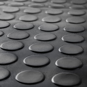 Macro close-up of the raised coin pattern texture on a black anti-slip rubber garage flooring mat.