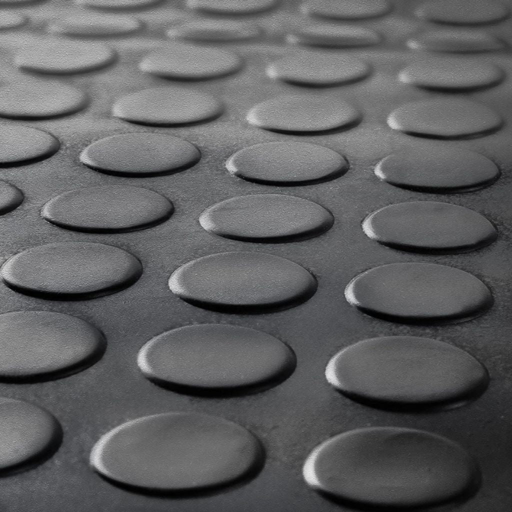 Macro close-up of the raised coin pattern texture on a black anti-slip rubber garage flooring mat.