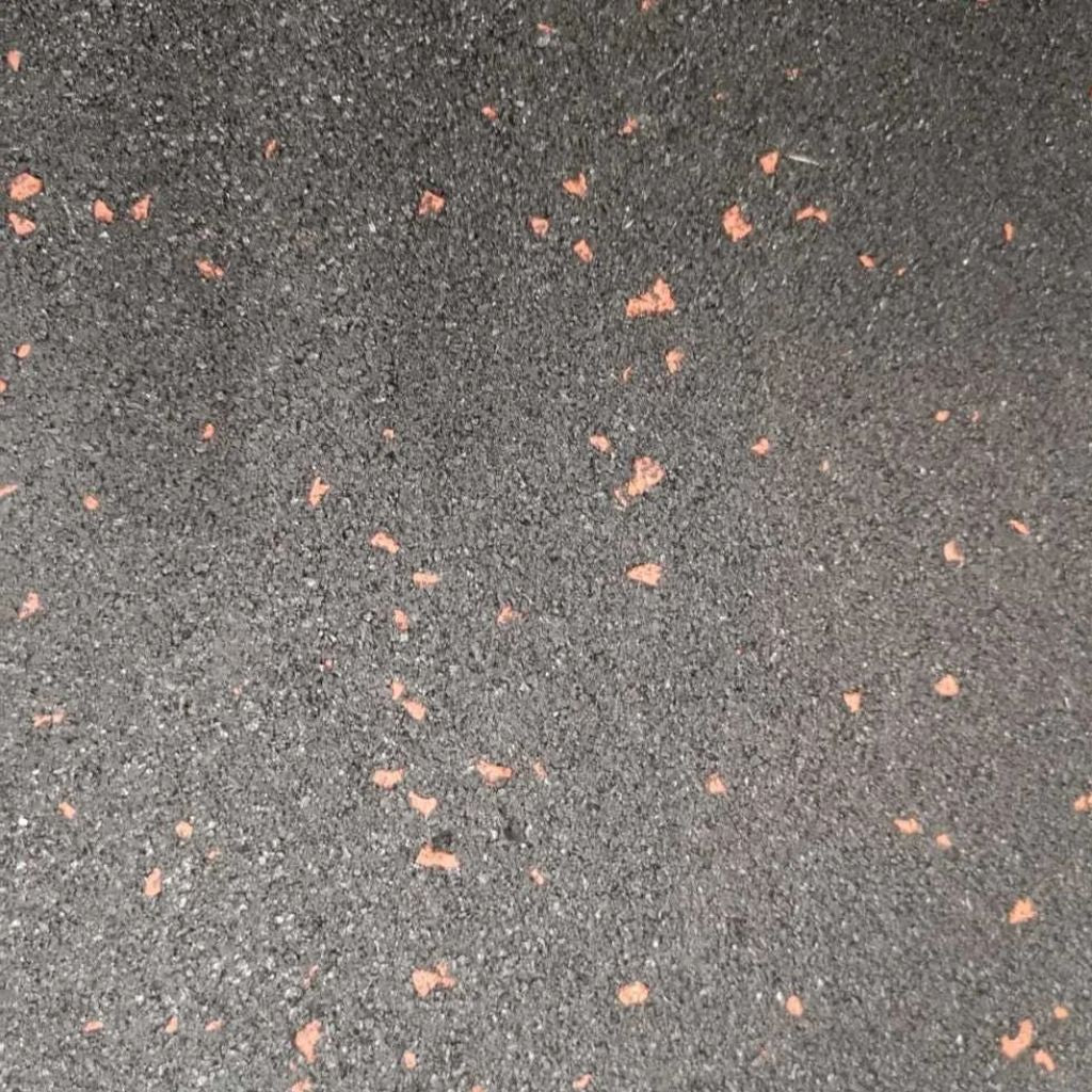 Top view texture of a black fine crumb rubber gym mat surface highlighting the burnt orange fleck design.