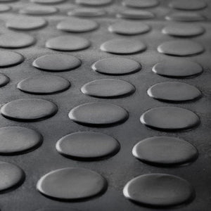 Close-up of the raised coin stud penny pattern on a black anti-slip rubber garage floor mat.