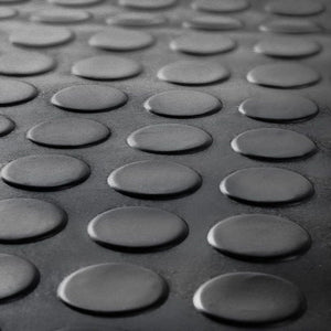 Low-perspective macro close-up of the raised anti-slip coin pattern on a black rubber floor mat.