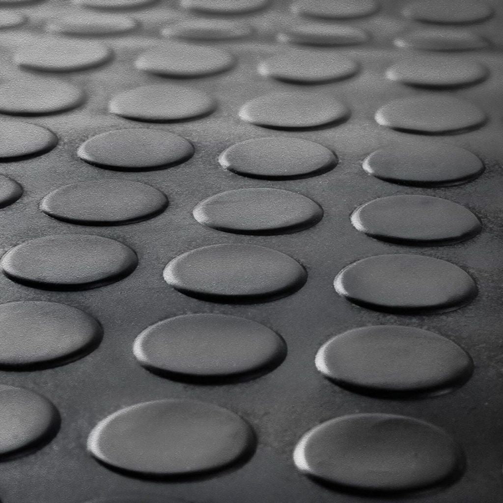 Low-perspective macro close-up of the raised anti-slip coin pattern on a black rubber floor mat.