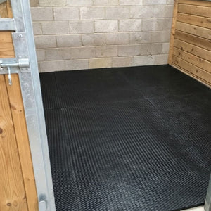 Perspective view from the entrance showing black cushioned EVA horse floor matting laid out across a horse stall.