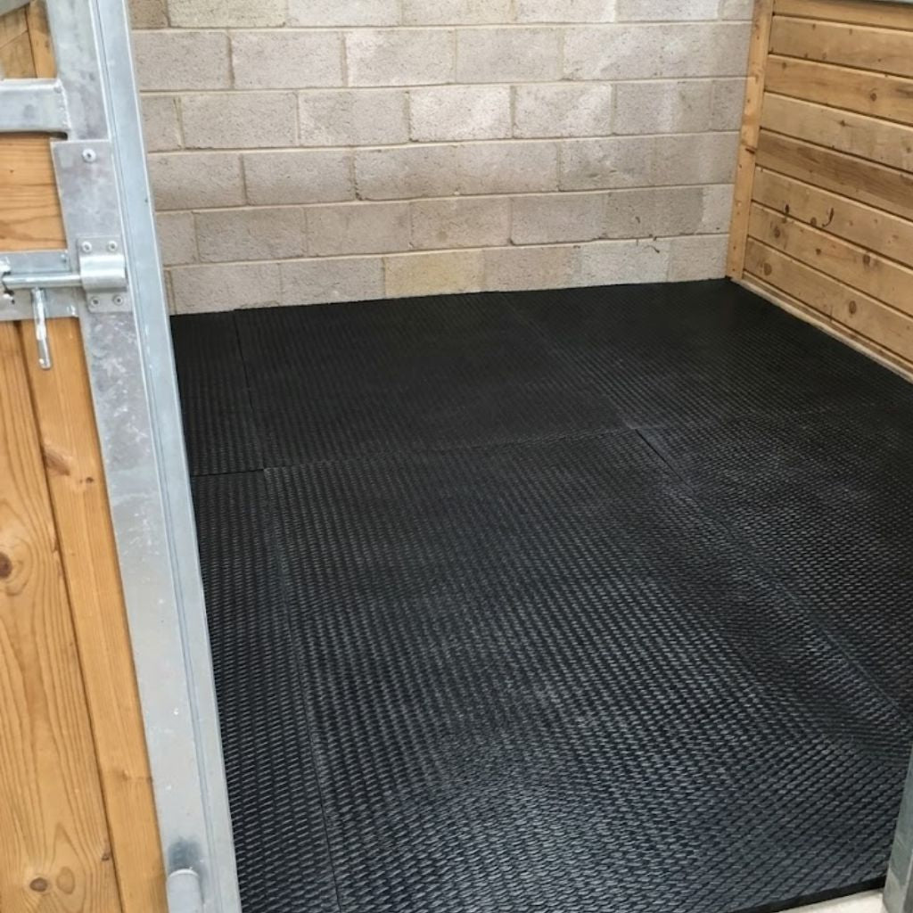 Perspective view from the entrance showing black cushioned EVA horse floor matting laid out across a horse stall.