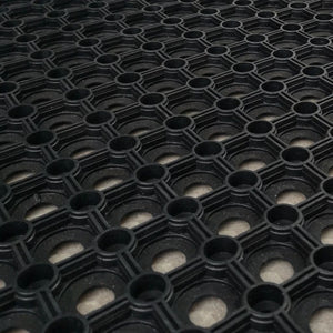 Angled close-up view of the open ring honeycomb structure of a black rubber gateway mat.