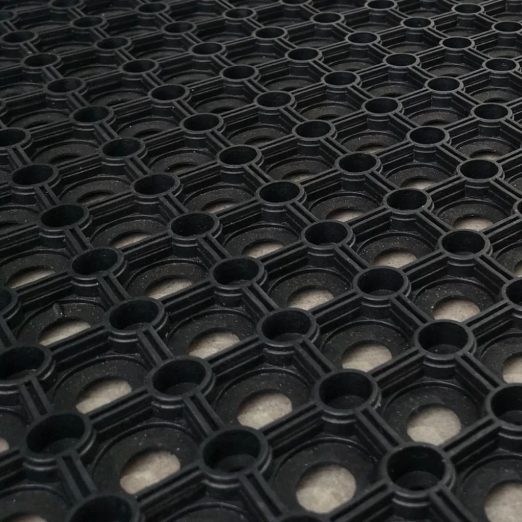 Angled close-up view of the open ring honeycomb structure of a black rubber gateway mat.