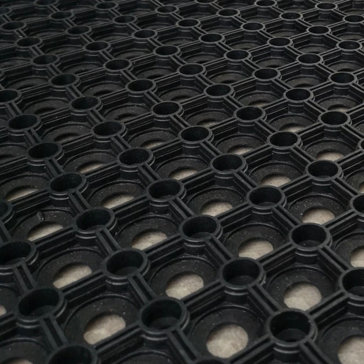 Angled close-up view of the open ring honeycomb structure of a black rubber gateway mat.
