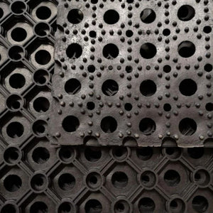 Close-up of a heavy duty black rubber grass mat showing the raised non-slip bobble texture and drainage holes.
