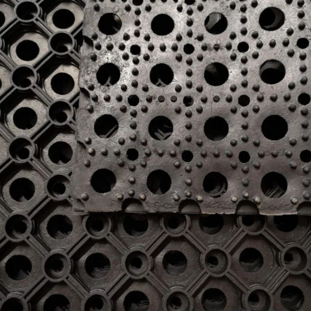 Close-up of a heavy duty black rubber grass mat showing the raised non-slip bobble texture and drainage holes.