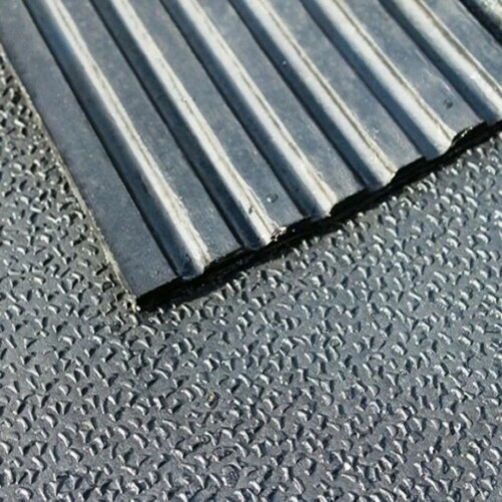 A close-up view of a 12mm thick heavy-duty rubber stable mat showing a textured amoebic finish surface layered over linear drainage grooves.