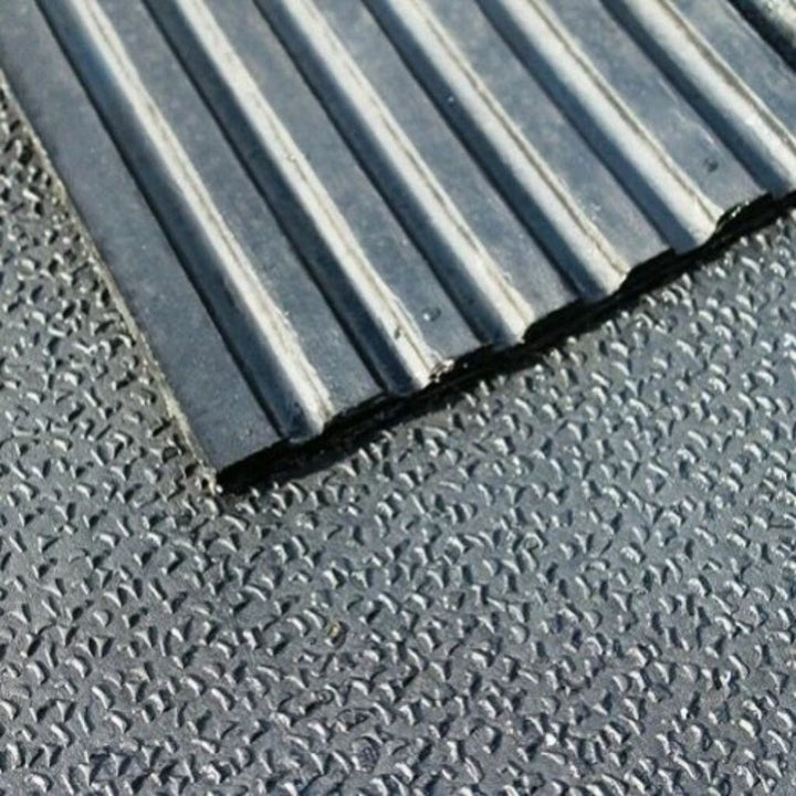 A close-up view of a 12mm thick heavy-duty rubber stable mat showing a textured amoebic finish surface layered over linear drainage grooves.