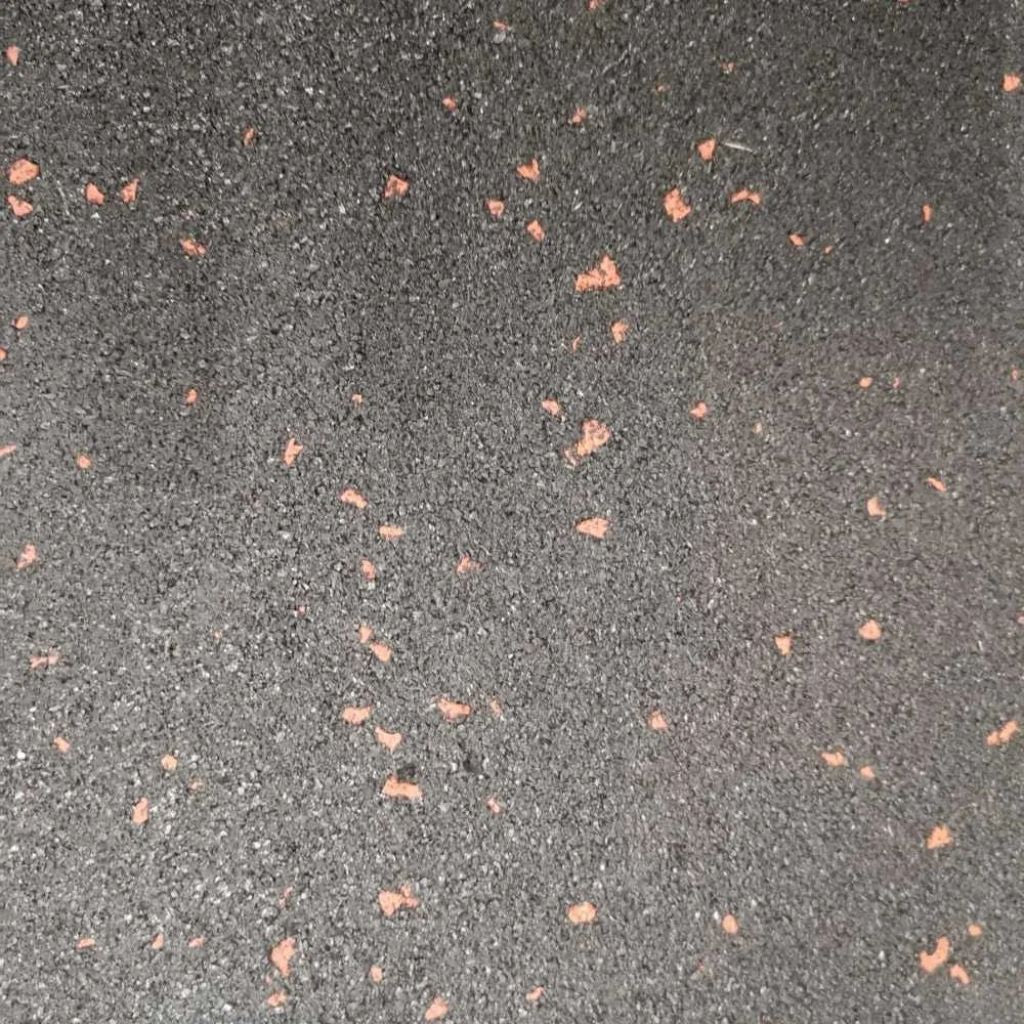 A flat top-down close-up of a black rubber gym floor tile featuring a slip-resistant textured surface with red EPDM flecks.